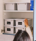 Person organizing storage bins labeled with names on a shelf.